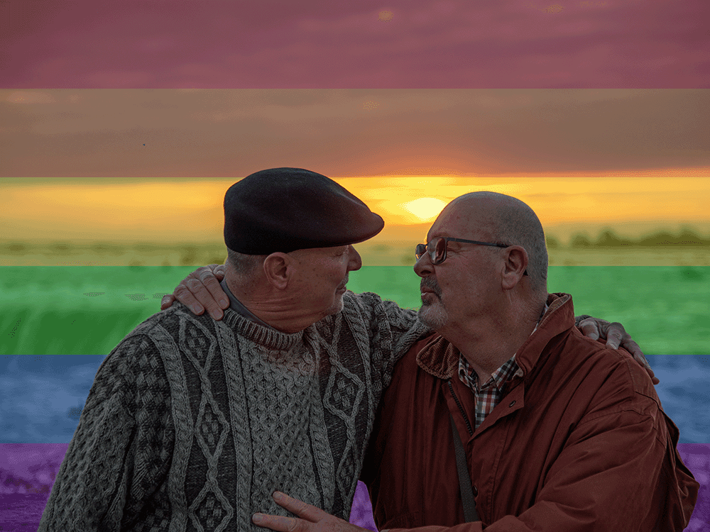Married gay senior citizens embrace and lean in for a kiss outdoors at sunrise in front of Niagara Falls. A muted rainbow flag overlay is in the background